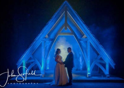 Bride and groom holding hands under a blue-lit wooden arch at Highley Manor